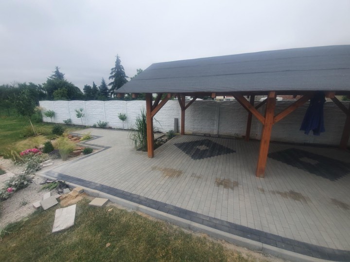 Taras z szarej kostki brukowej pod drewnianą altaną, otoczony trawnikiem
